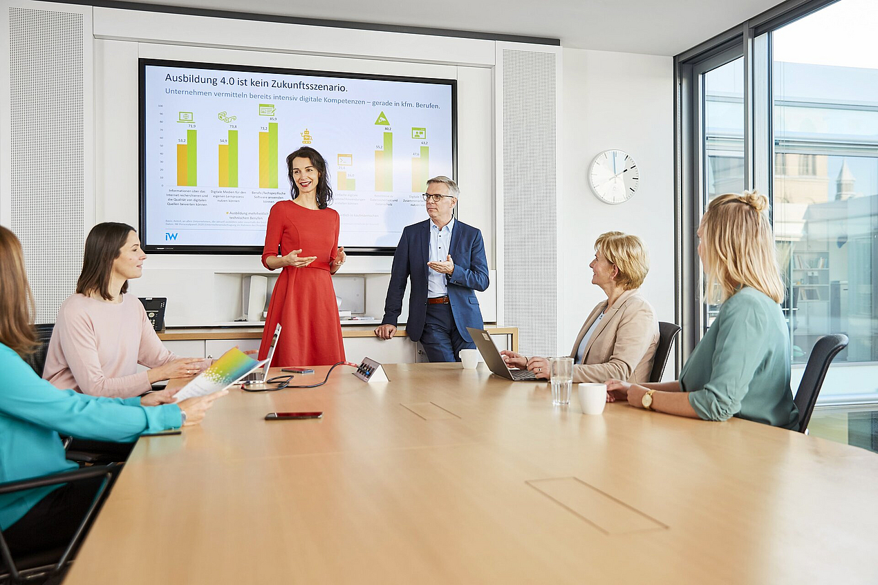 Ein Teil des KOFA-Teams ist in einem Besprechungsraum. Zwei Personen stehen, vier sitzen und schauen in Richtung Präsentation.