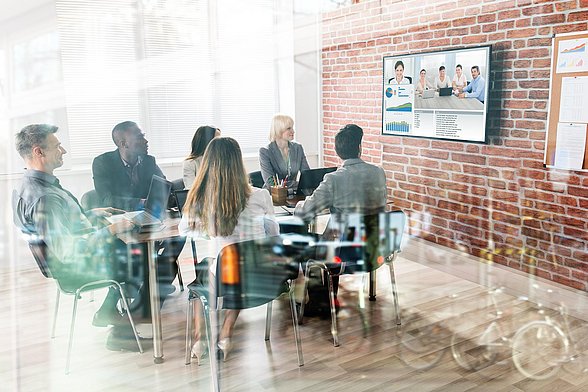 Menschen sitzen in einem Besprechungsraum und führen eine Videokonferenz