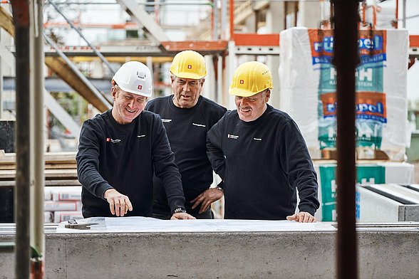 Drei Männer stehen auf einer Baustelle und besprechen Baupläne