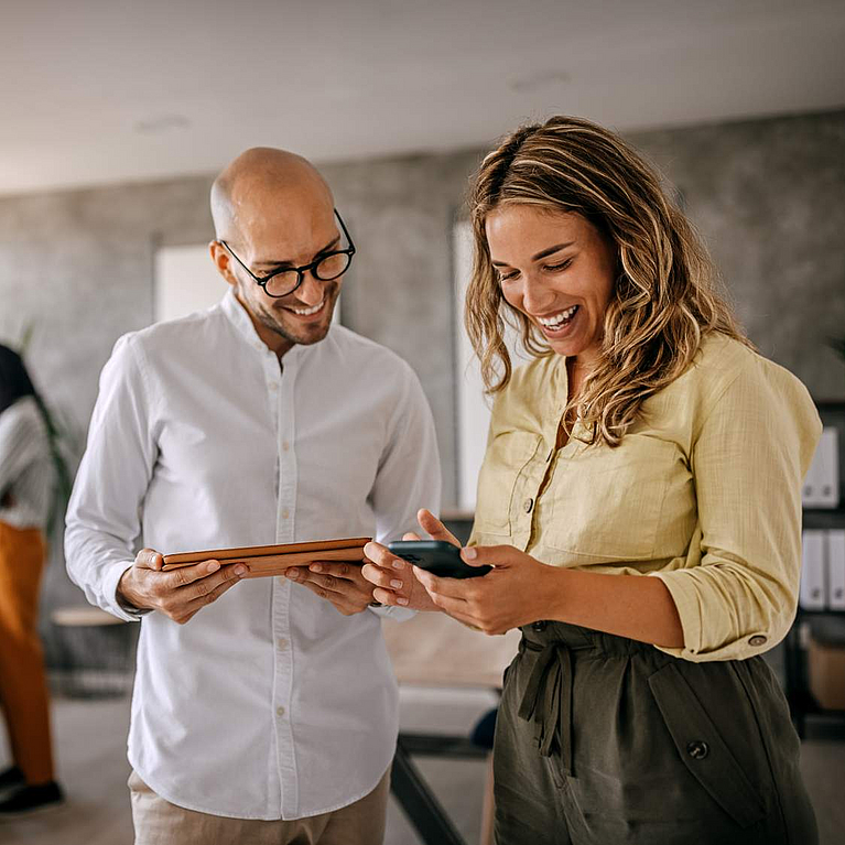© mixetto -istock.com Mann und Frauen schauen lächelnd auf Smartphone und Tablet